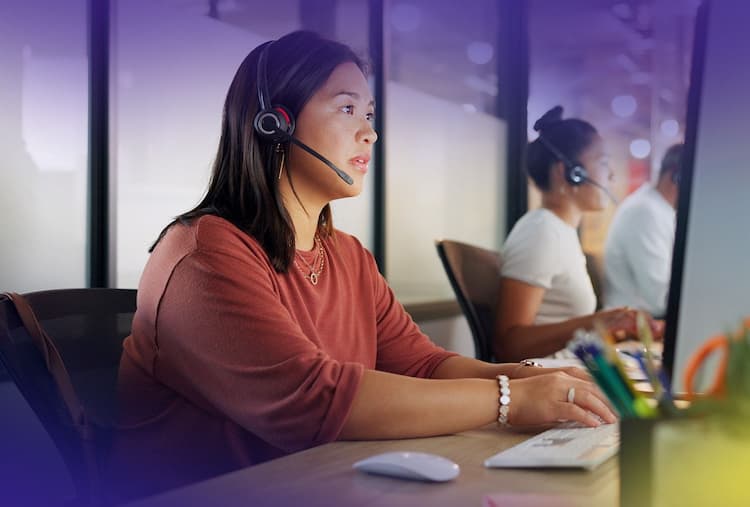 Two women sit at computers with headsets on while on calls.